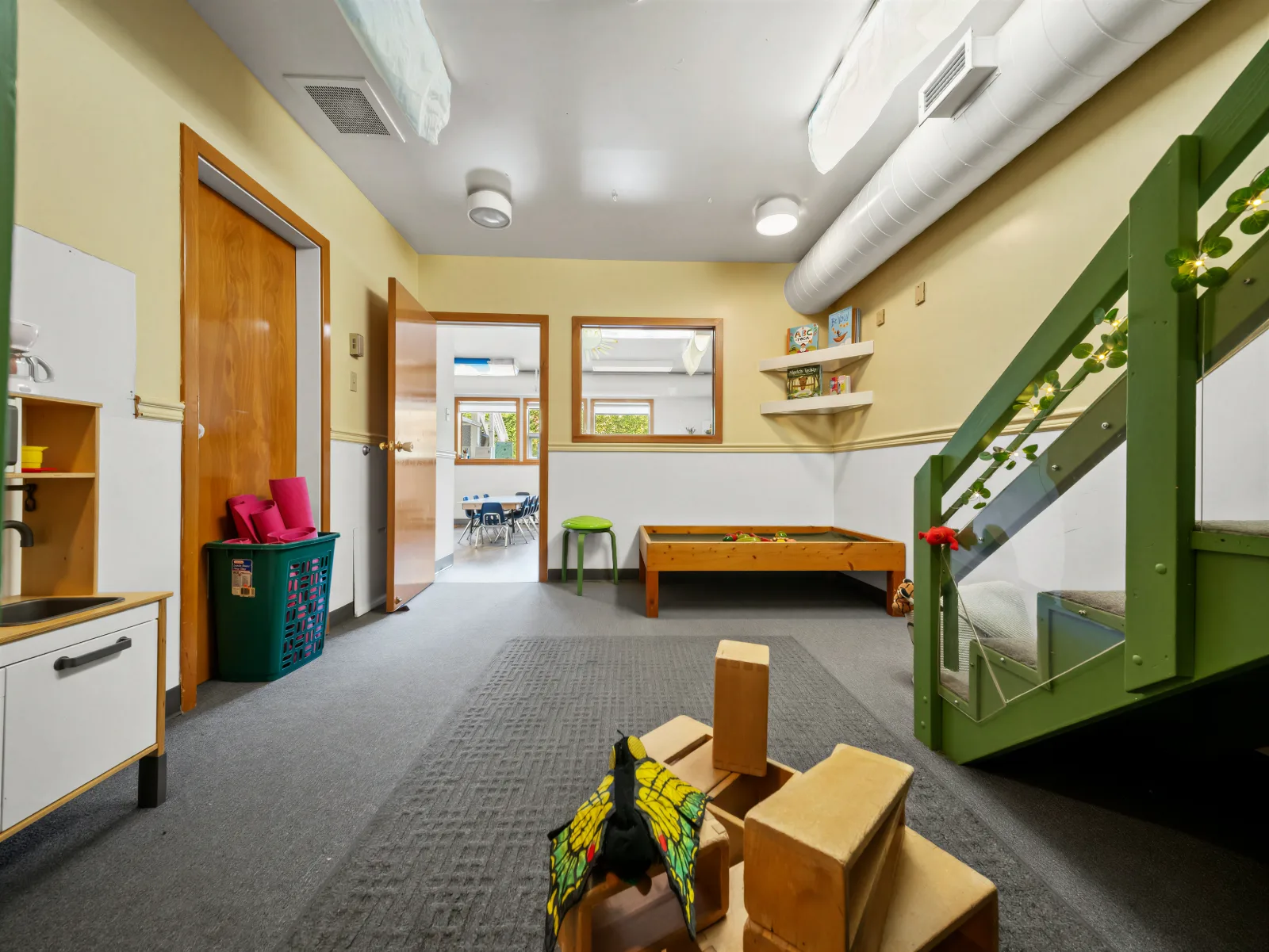 A warm yellow play space with a green reading loft and water table